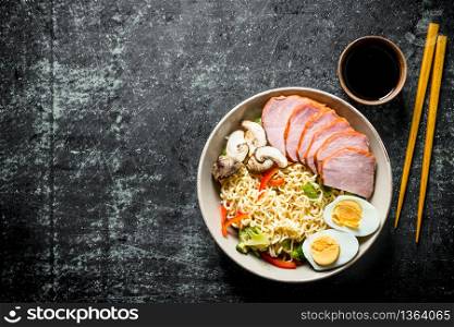Instant noodles with vegetables, egg, ham, soy sauce and chopsticks. On dark rustic background. Instant noodles with vegetables, egg, ham, soy sauce and chopsticks.