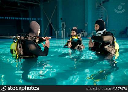 Instructor and two divers in suits, lesson in diving school. Teaching people to swim underwater with scuba gear, indoor swimming pool interior on background, group training. Instructor and two divers, lesson in diving school