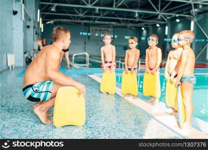 Instructor training children in the pool. Boys with swimming goggles ready for swimming and stands near water. Healthy activity in pool. Sportive kids activity in modern sport center with pool.. Instructor training children in the pool