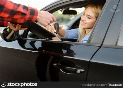 Instructor with checklist gives the keys to student in car, examination or lesson in driving school. Man teaching lady to drive vehicle, exam. Driver&rsquo;s license education. Instructor gives the keys to student in car, exam