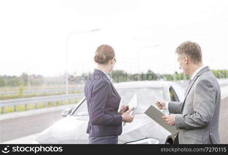 Insurance agent discussing with businesswoman while pointing at breakdown car against sky