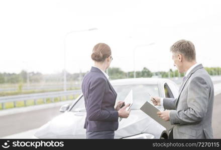 Insurance agent discussing with businesswoman while pointing at breakdown car against sky