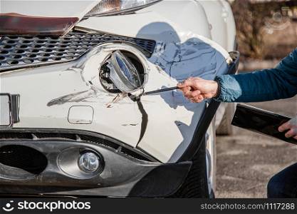 Insurance agent will examine and examine the damage to the car after an accident. Inspection of the car after an accident on the road. The front fender and right headlight are broken, damaged and scratched on the bumper.. Insurance agent will examine and examine the damage to the car after an accident. Inspection of the car after an accident on the road.