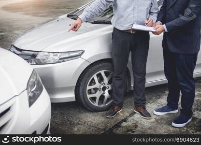 Insurance agent writing on clipboard while examining car after accident claim being assessed and processed