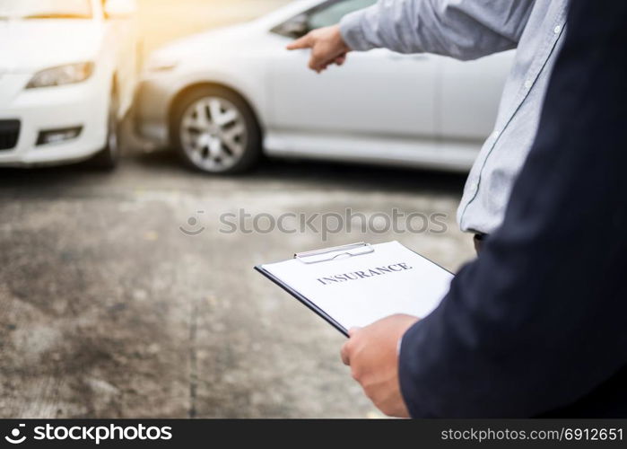 Insurance agent writing on clipboard while examining car after accident claim being assessed and processed