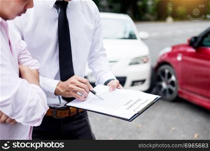 Insurance agent writing on clipboard while examining car after accident claim being assessed and processed