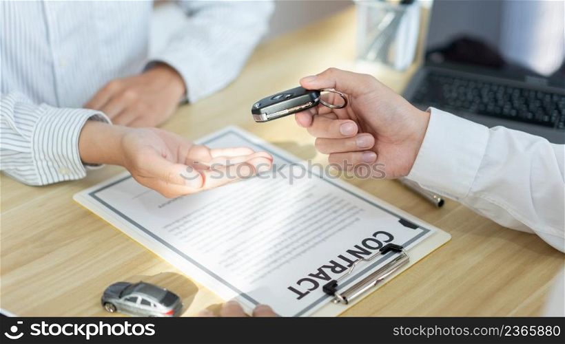 Insurance concept the car dealership giving a car key to his customer after signing the contract .