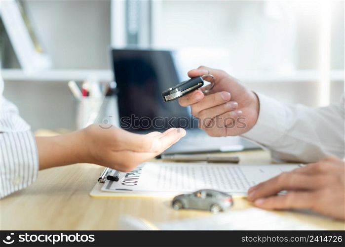 Insurance concept the car dealership giving a car key to his customer after signing the contract .