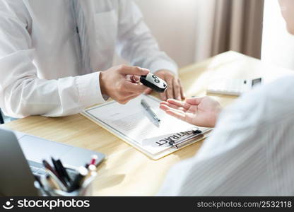 Insurance concept the car dealership giving a car key to his customer after signing the contract .