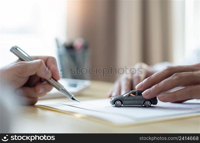 Insurance concept the customer signing his name on the contract while the dealer giving more details.