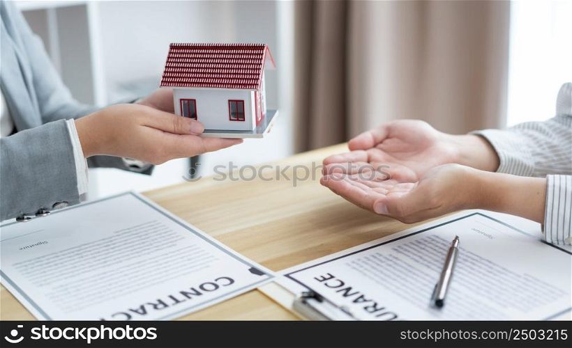 Insurance concept the estate agent holding a house model and giving it to his client.