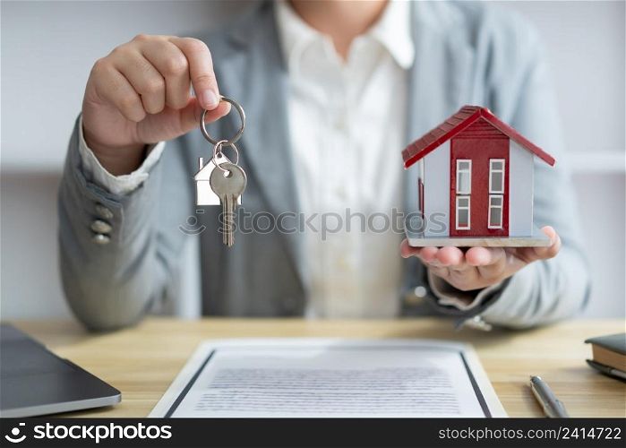 Insurance concept the real estate representative holding a house key on the right hand and the house model on the left hand.