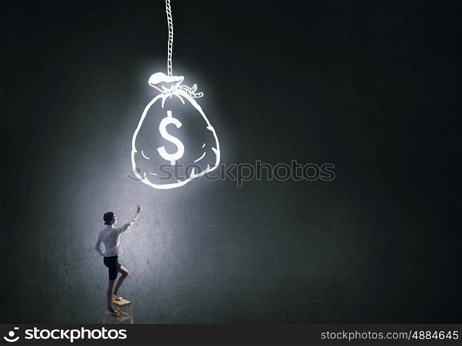 Intention to become rich. Young attractive businesswoman standing on chair and reaching money bag