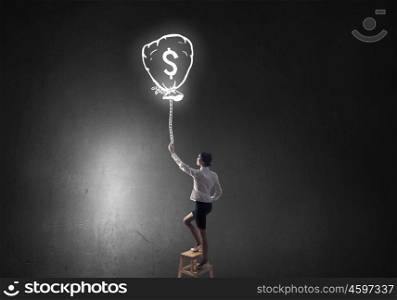 Intention to become rich. Young attractive businesswoman standing on chair with dollar balloon in hand