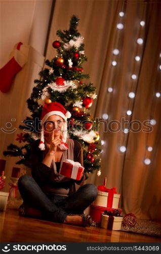 Interested girl near Christmas tree with present box trying to guess what&rsquo;s inside&#xA;