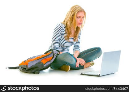 Interested pretty girl sitting on floor with backpack and looking on laptop isolated on white &#xA;