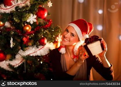 Interested woman near Christmas tree shaking present box trying to guess what&rsquo;s inside&#xA;