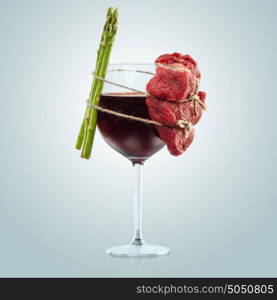 Interesting composition of meat and plants wiredly connected over the wine glass.