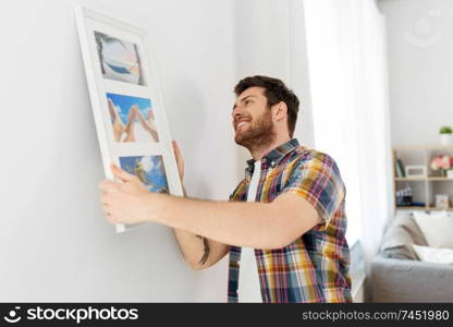 interior decoration and renovation concept - smiling man hanging picture in frame to wall at home. man hanging picture in frame to wall at home