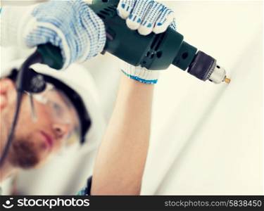 interior design and home renovation concept - man in helmet with electric drill making hole in wall