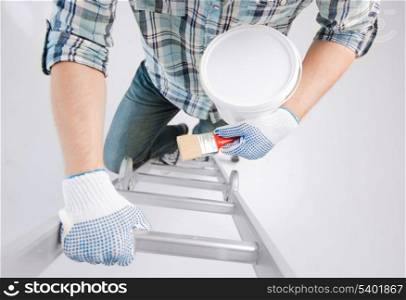 interior design and home renovation concept - man with paintbrush and paint pot climbing ladder