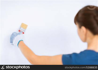 interior design and home renovation concept - woman with paintbrush colouring the wall