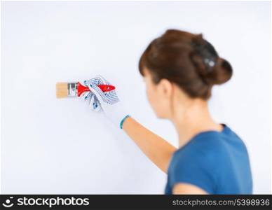 interior design and home renovation concept - woman with paintbrush colouring the wall