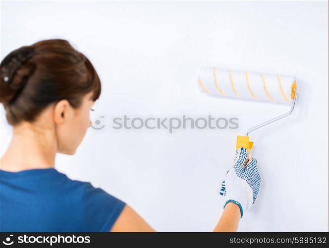 interior design and home renovation concept - woman with roller and paint colouring the wall. woman with roller and paint colouring the wall