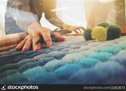 Interior designer hand chosing carpet sample with blank new modern computer laptop and pro digital tablet with material board on wooden desk as concept