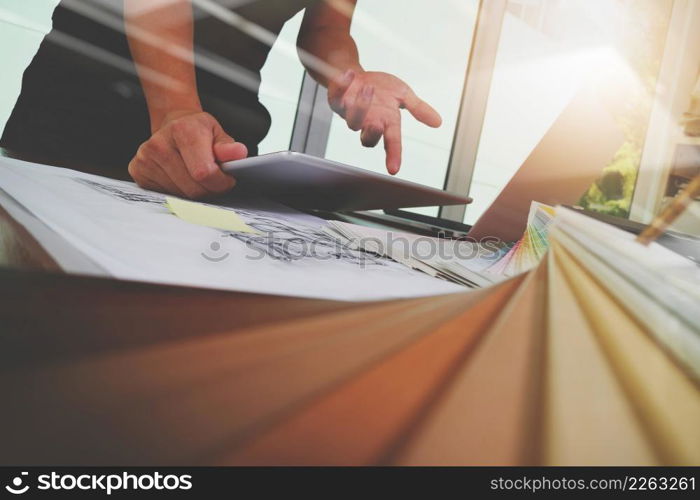 Interior designer hand working with new modern computer laptop and pro digital tablet with sample material board on wooden desk as concept