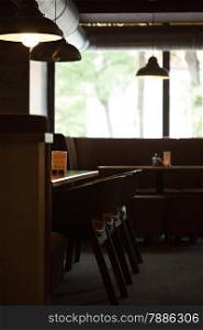 Interior of an empty cafe. Cozy place with wooden chairs and tables and sofa by the big window