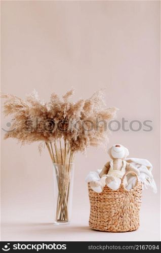 Interior of house of Natural accessories for home decor - dried plants in glass vase, wicker basket with teddy rabbit and plaid. Scandinavian cozy decor. copy space.. Interior of house of Natural accessories for home decor - dried plants in glass vase, wicker basket with teddy rabbit and plaid. Scandinavian cozy decor. copy space