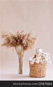 Interior of house of Natural accessories for home decor - dried plants in glass vase, wicker basket with teddy rabbit and plaid. Scandinavian cozy decor. copy space.. Interior of house of Natural accessories for home decor - dried plants in glass vase, wicker basket with teddy rabbit and plaid. Scandinavian cozy decor. copy space
