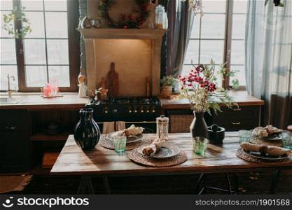 Interior of kitchen. Served dining table with plates glasses floral decor. Cutlery and glassware. Preparation for festive dinner. Table setting for family supper