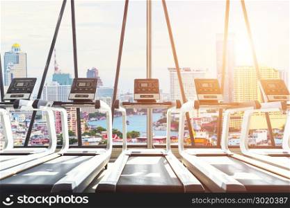Interior of modern treadmills in gym at sunrise with view of city outside. Fitness background concept.