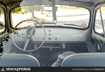 Interior of small white vintage car on the street. No people. White steering wheel. View through the window. Travel concept with car.