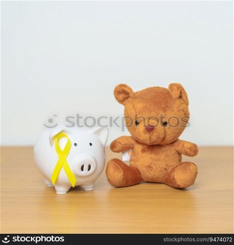 International Childhood Cancer Aware≠ss month, Children toy with golden yellow color Ribbon with Piggy Bank for Donation, Charity, C&aign, Mo≠y Saving, Fund and World cancer day concept