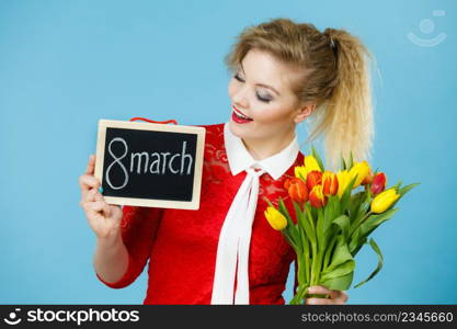 International women day. Beautiful woman blonde hair fashion make up holding red yellow tulips and frame board with message 8 march. On blue. Woman holds tulips, board with text 8 march