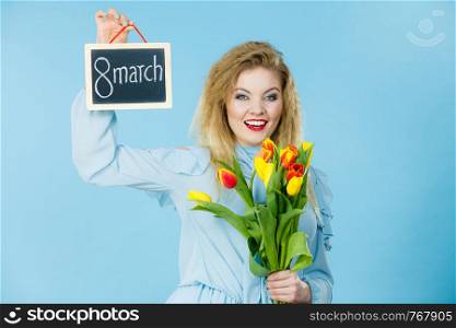 International women day. Beautiful woman blonde hair fashion make up holding red yellow tulips and frame board with message 8 march. On blue. Woman holds tulips, board with text 8 march