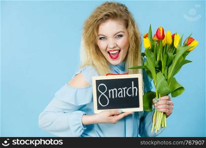 International women day. Beautiful woman blonde hair fashion make up holding red yellow tulips and frame board with message 8 march. On blue. Woman holds tulips, board with text 8 march
