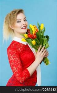 International women day, eight march. Beautiful portrait of pretty woman blonde hair with red yellow tulips, fashion make up, elegant outfit. Mother day. On blue. Pretty woman with red yellow tulips bunch