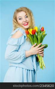 International women day, eight march. Beautiful portrait of pretty woman blonde hair with red yellow tulips, fashion make up, elegant dress. Mother day. On blue. Pretty woman with red yellow tulips bunch