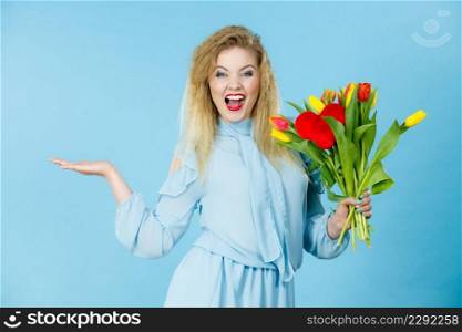 International women day, eight march. Lovely woman blonde girl with red yellow tulips, elegant dress holding open empty hand, copy space for product. On blue. woman with tulips bunch, open hand