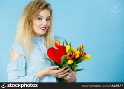 International women or valentine day. Beautiful woman blonde hair fashion make up holding tulips bunch and red heart sign. On blue. Woman holds tulips and red heart