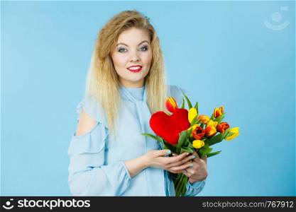 International women or valentine day. Beautiful woman blonde hair fashion make up holding tulips bunch and red heart sign. On blue. Woman holds tulips and red heart