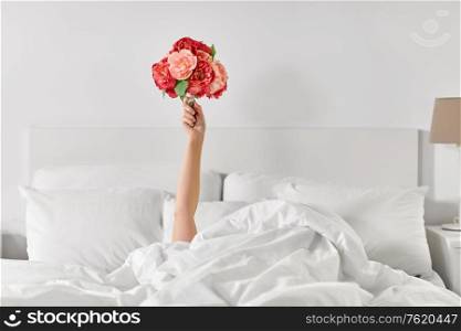 international women&rsquo;s day, comfort and morning concept - hand of young woman lying in bed with bunch of flowers at bedroom. hand of woman lying in bed with bunch of flowers