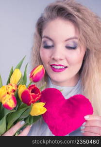 International womens or valentines day. Attractive grateful woman blonde hair holding tulips bunch and red heart sign. On grey. Woman holds tulips and red heart