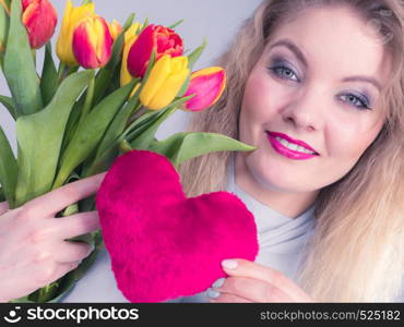 International womens or valentines day. Attractive grateful woman blonde hair holding tulips bunch and red heart sign. On grey. Woman holds tulips and red heart