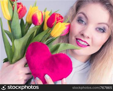 International womens or valentines day. Attractive grateful woman blonde hair holding tulips bunch and red heart sign. On grey. Woman holds tulips and red heart