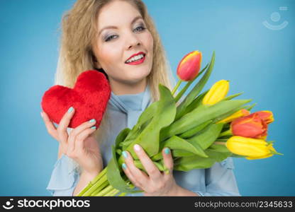 International womens or valentines day. Attractive happy woman blonde hair fashion make up holding tulips bunch and red heart sign. On blue. Woman holds tulips and red heart